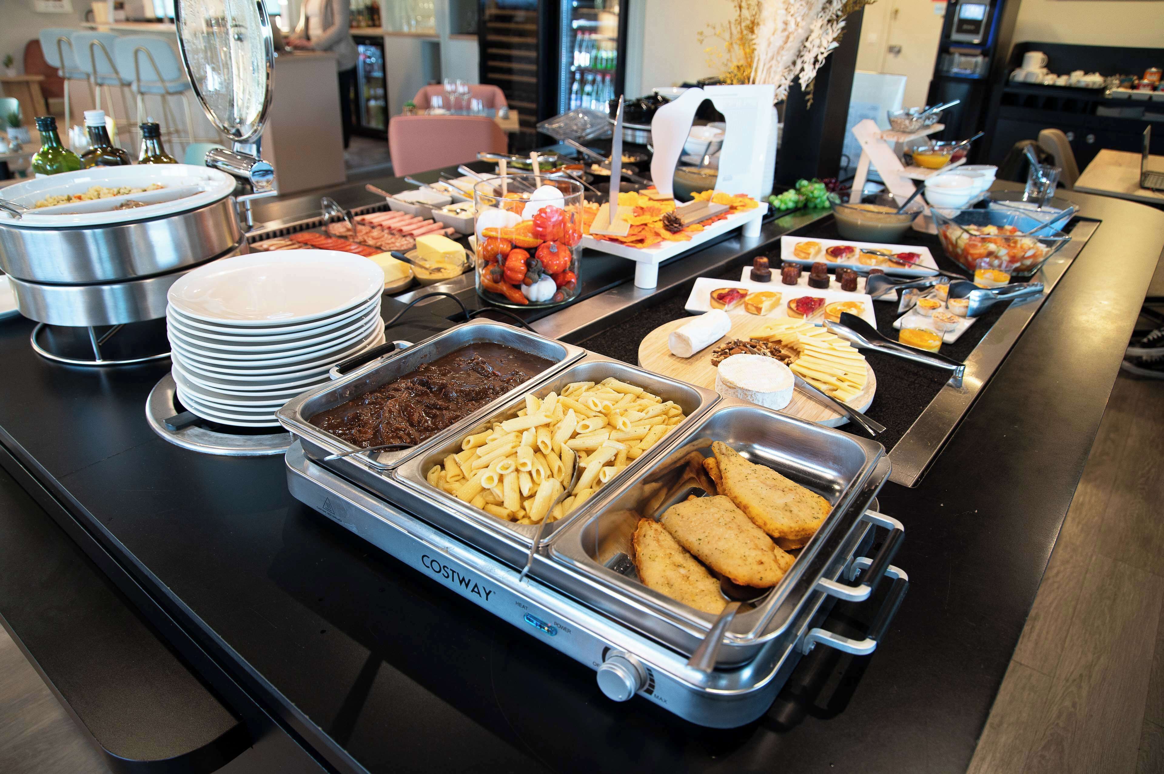 A buffet with various food options including pasta, bread, and desserts.