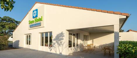 A hotel with a sign reading "Sure Hotel by BEST WESTERN," a covered outdoor seating area, and a paved driveway.