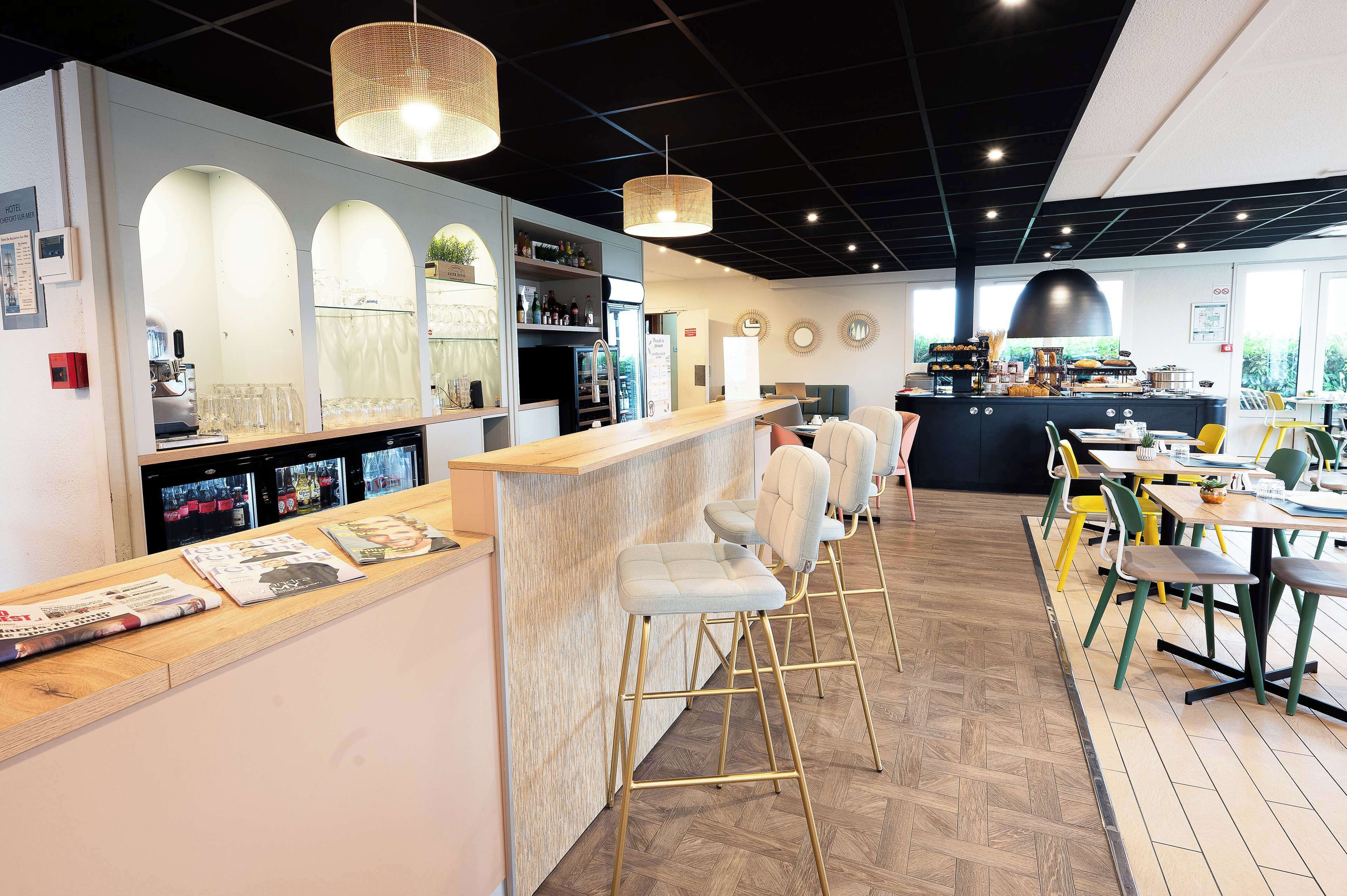 A modern bar area with a wooden counter, bar stools, and a seating area with tables and chairs.