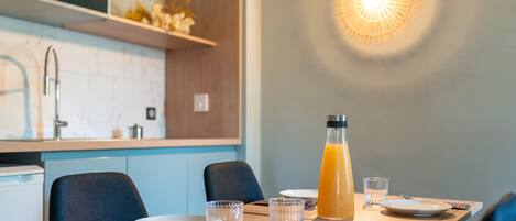 A dining table with plates, glasses, and a juice bottle in a modern kitchen with a light fixture above.