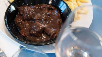 A plate with a bowl of beef stew and pasta, a glass of wine, and a fork on a table with a blue placemat.