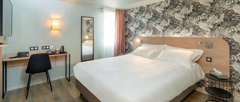 A hotel room with a bed, a desk with a chair, a telephone, a lamp, and a mirror.