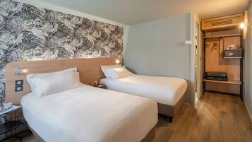 Hotelkamer met twee bedden, een houten hoofdbord, een tafeltje met een stoel, een kledingkast en een behang met patroon.