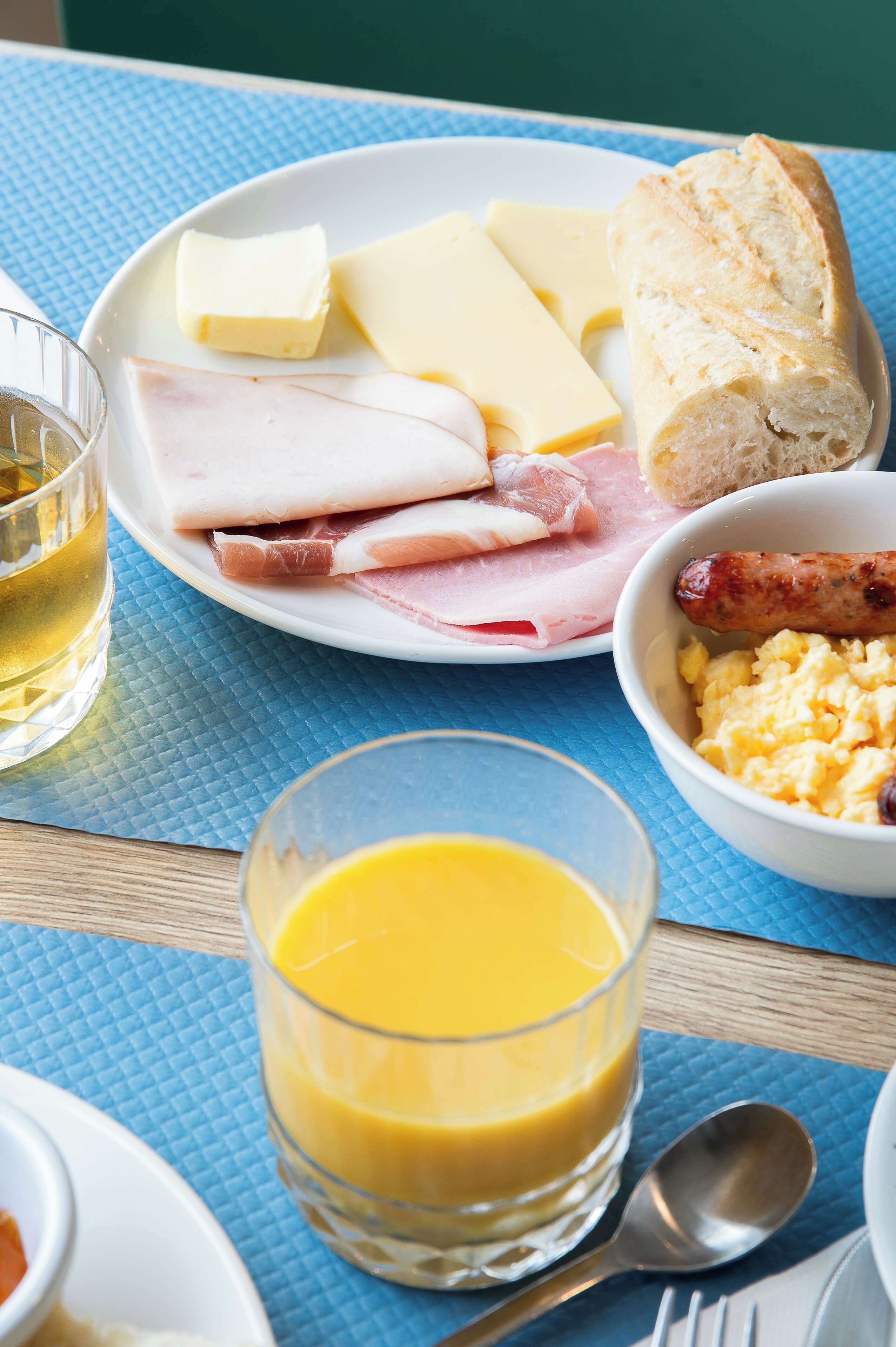 A breakfast plate with ham, cheese, sausage, bread, and scrambled eggs.