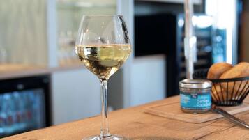 Una copa de vino blanco sobre una barra de madera, con una lata de cerveza y una cesta de pan al fondo.