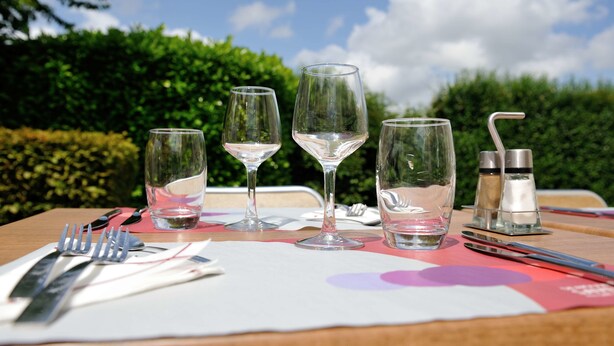 A table set with wine glasses, cutlery, and salt and pepper shakers, with a view of greenery and a clear sky in the background. - Hotel Campanile Bourges Nord- Saint Doulchard (Saint-Doulchard)