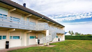 A multi-story building with a balcony, a covered entrance, and a well-maintained lawn. - Hotel Campanile Bourges Nord- Saint Doulchard (Saint-Doulchard)