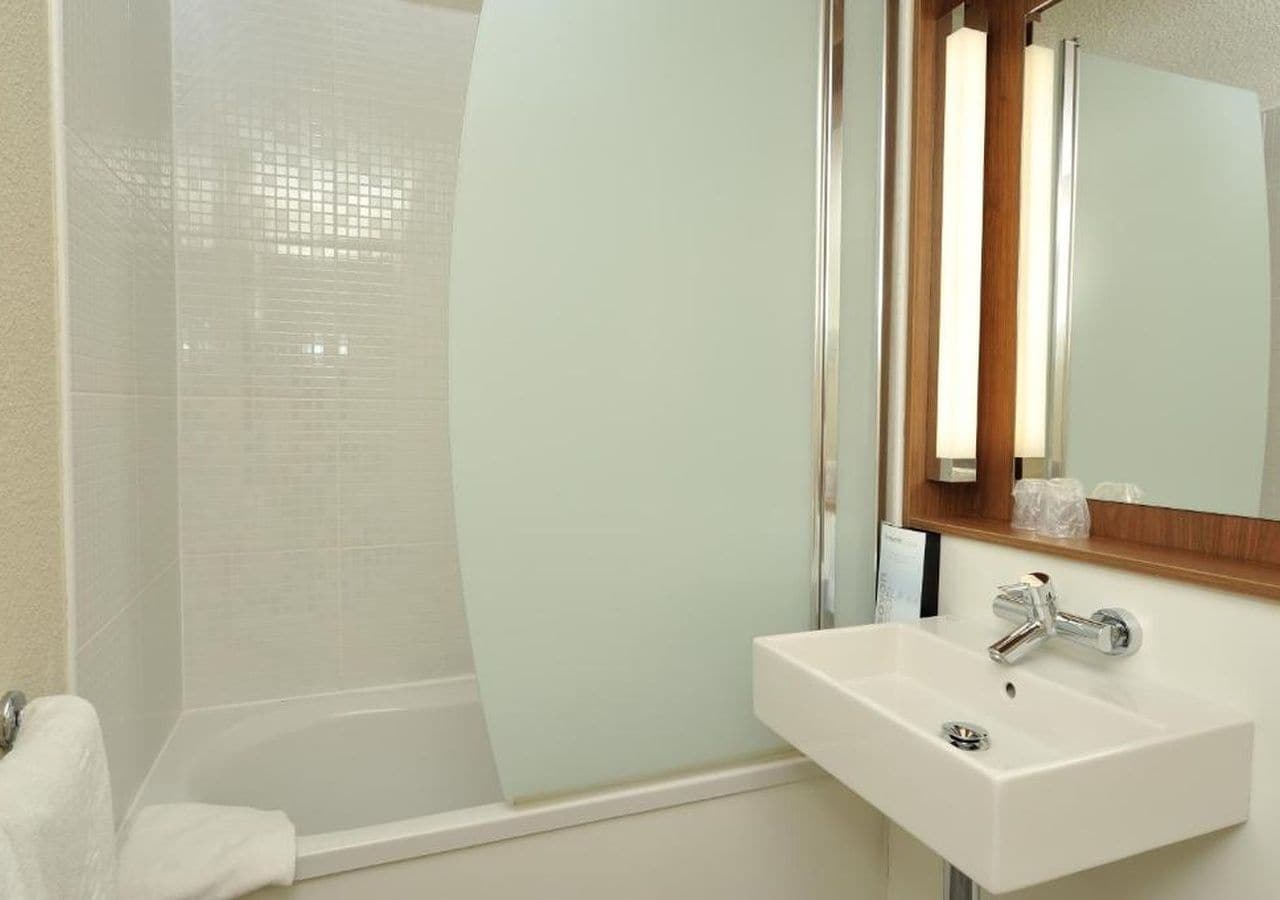 A bathroom with a glass shower enclosure, a white sink with a chrome faucet, and a mirror with a wooden frame.
