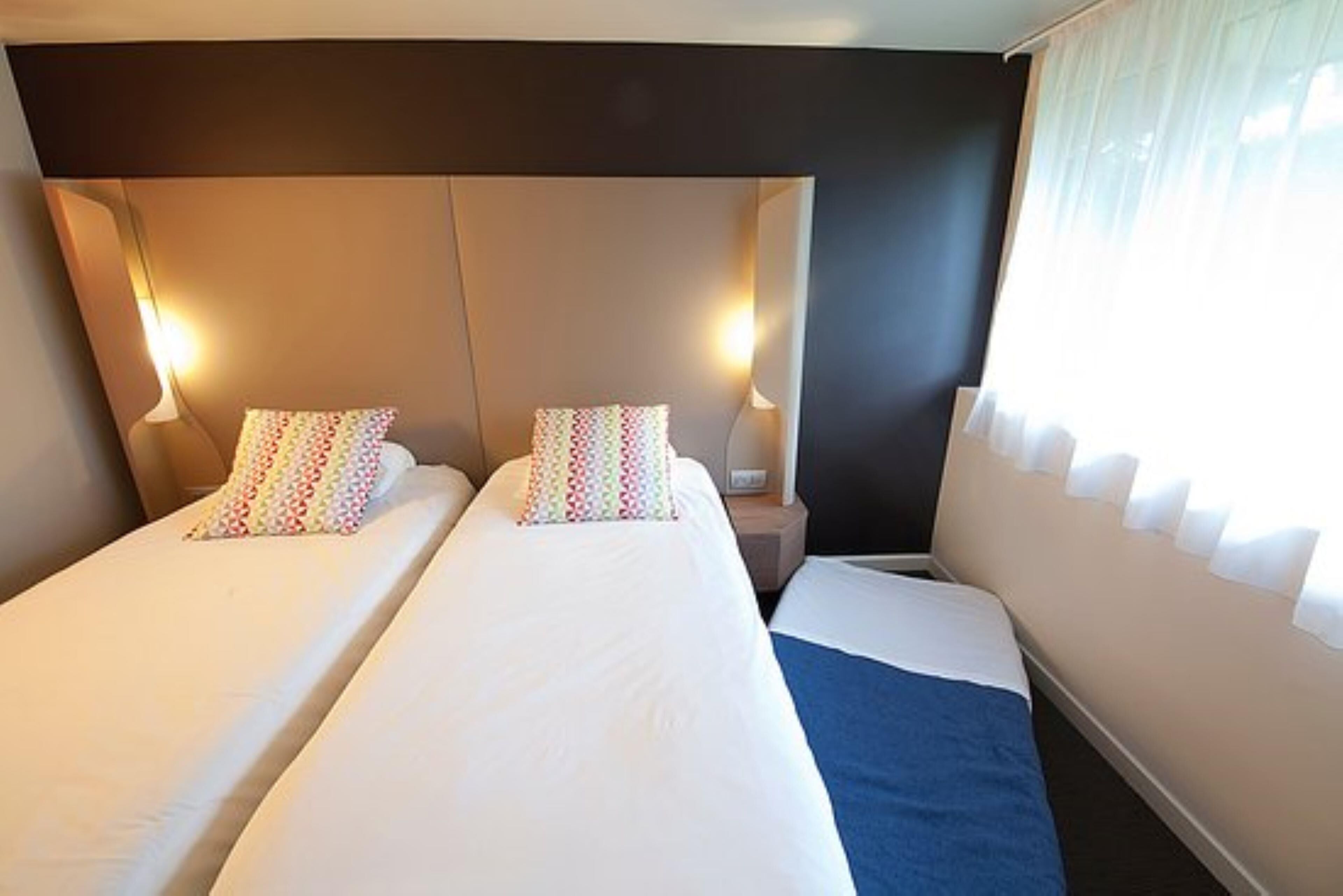 Habitación de hotel con dos camas, cada una con almohada y mesita de noche con lámpara.