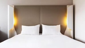 Una habitación de hotel moderna con una cama grande, dos lámparas de noche y una paleta de colores neutros.