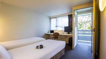 A hotel room with two single beds, a desk with a computer, a chair, and a door leading to an outdoor area.
