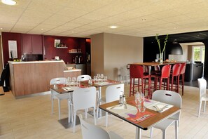 A modern restaurant with white chairs, wooden tables, and a bar area.
