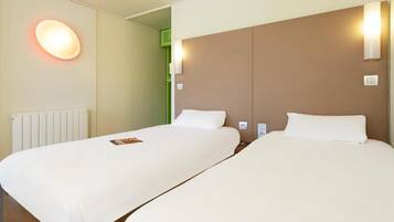 A hotel room with two beds, a radiator, and a wall-mounted light fixture.