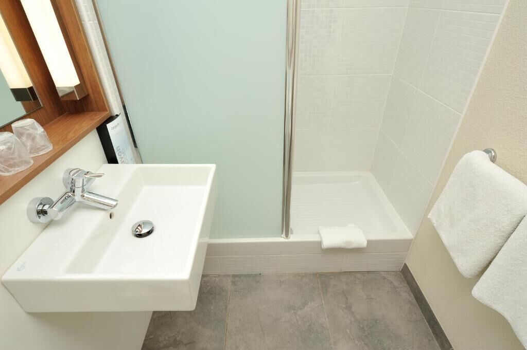 A bathroom with a white sink, a glass shower enclosure, and a white towel on the floor.