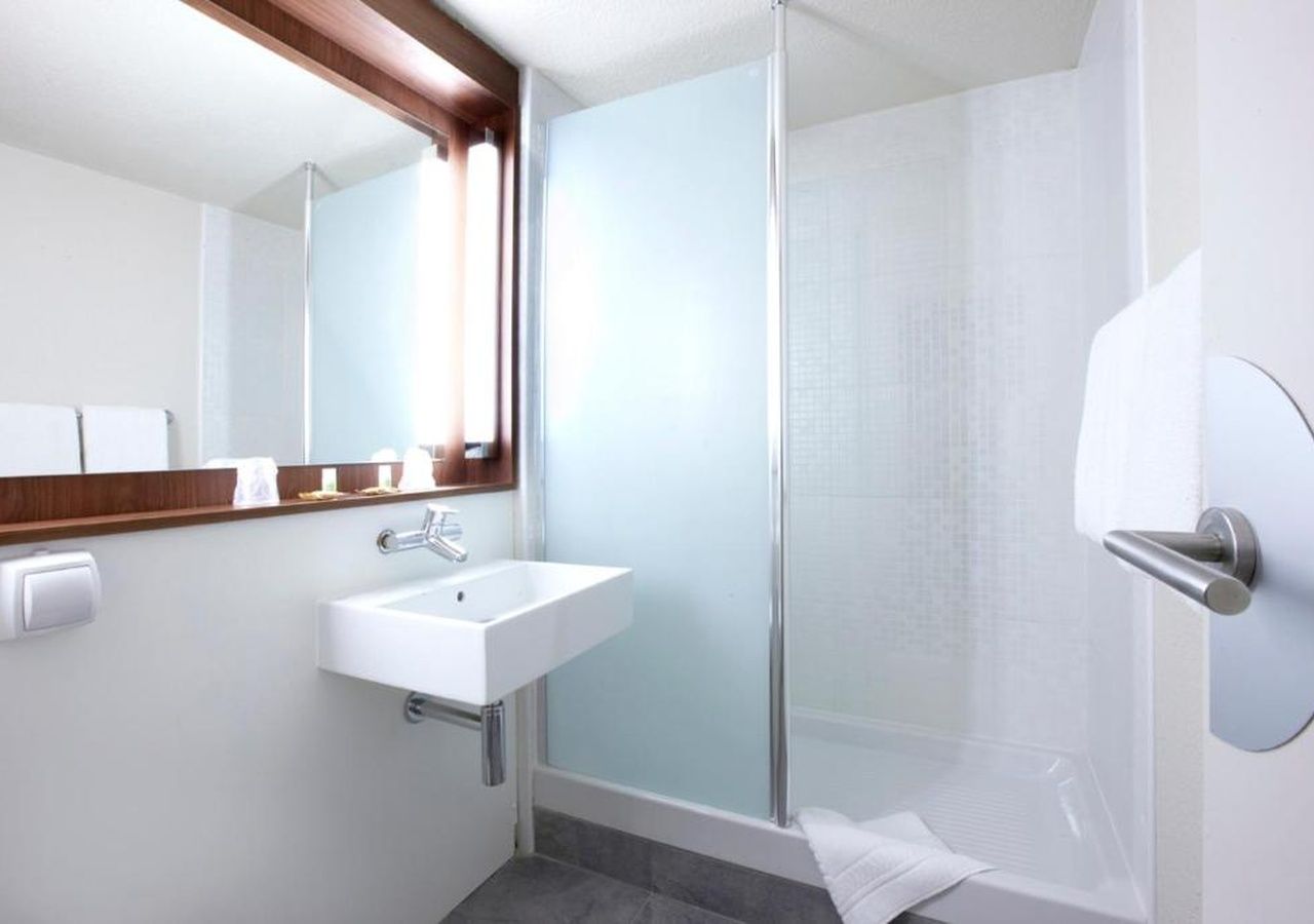 A modern bathroom with a glass shower enclosure, a white sink, and a mirror with a wooden frame.