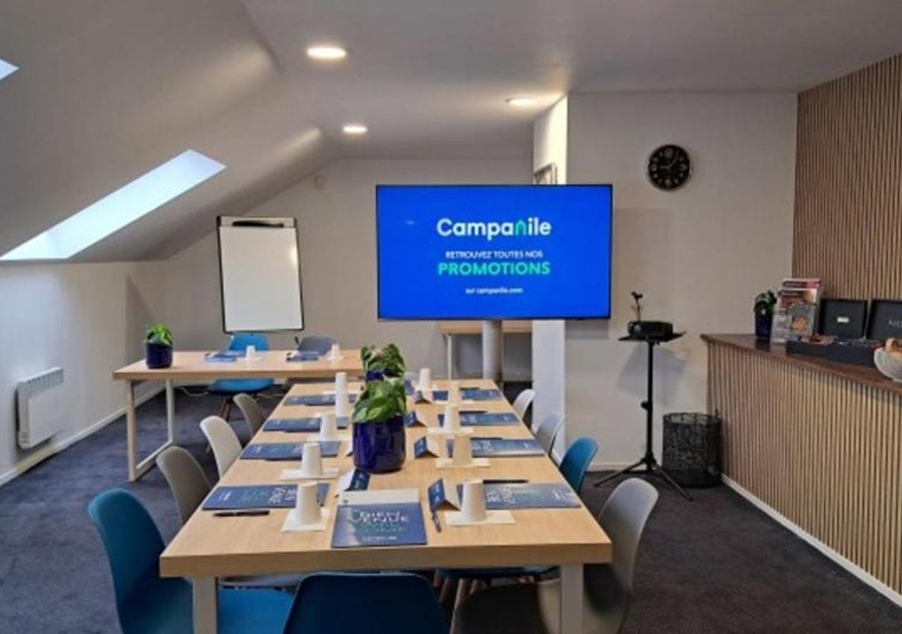 A conference room with a long table, chairs, a projector screen, and a clock on the wall.