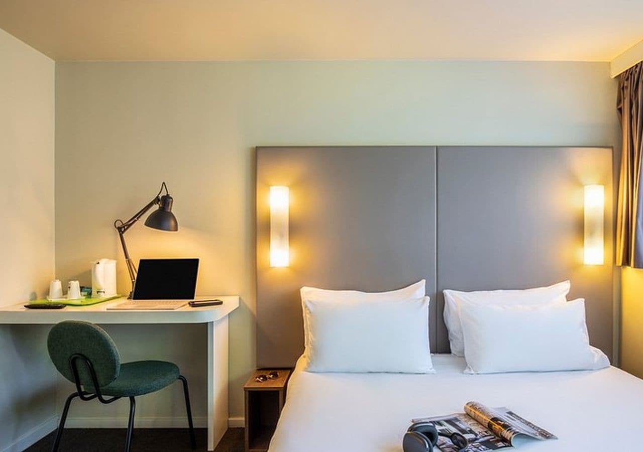 Habitación de hotel con cama, escritorio, computadora portátil, silla y lámparas de noche.