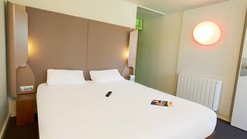 Une chambre d’hôtel avec un grand lit, une table de chevet, une lampe fixée au mur et un radiateur.