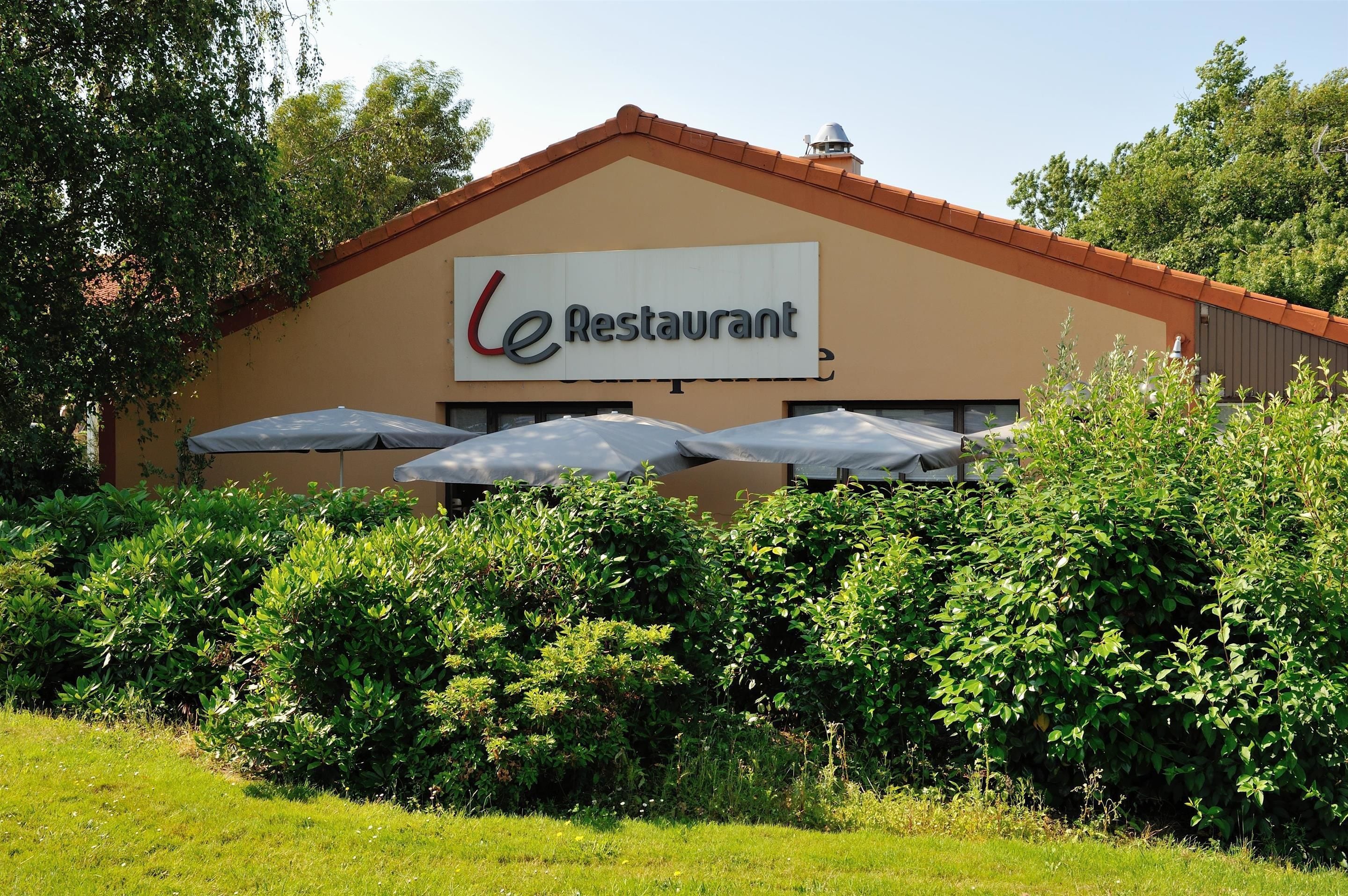 Un restaurant avec une enseigne indiquant « Le Restaurant » et des parasols à l’extérieur.