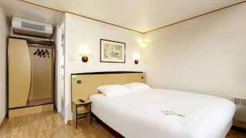 A hotel room with a large bed, a wooden wardrobe, a nightstand, and two wall-mounted lamps.