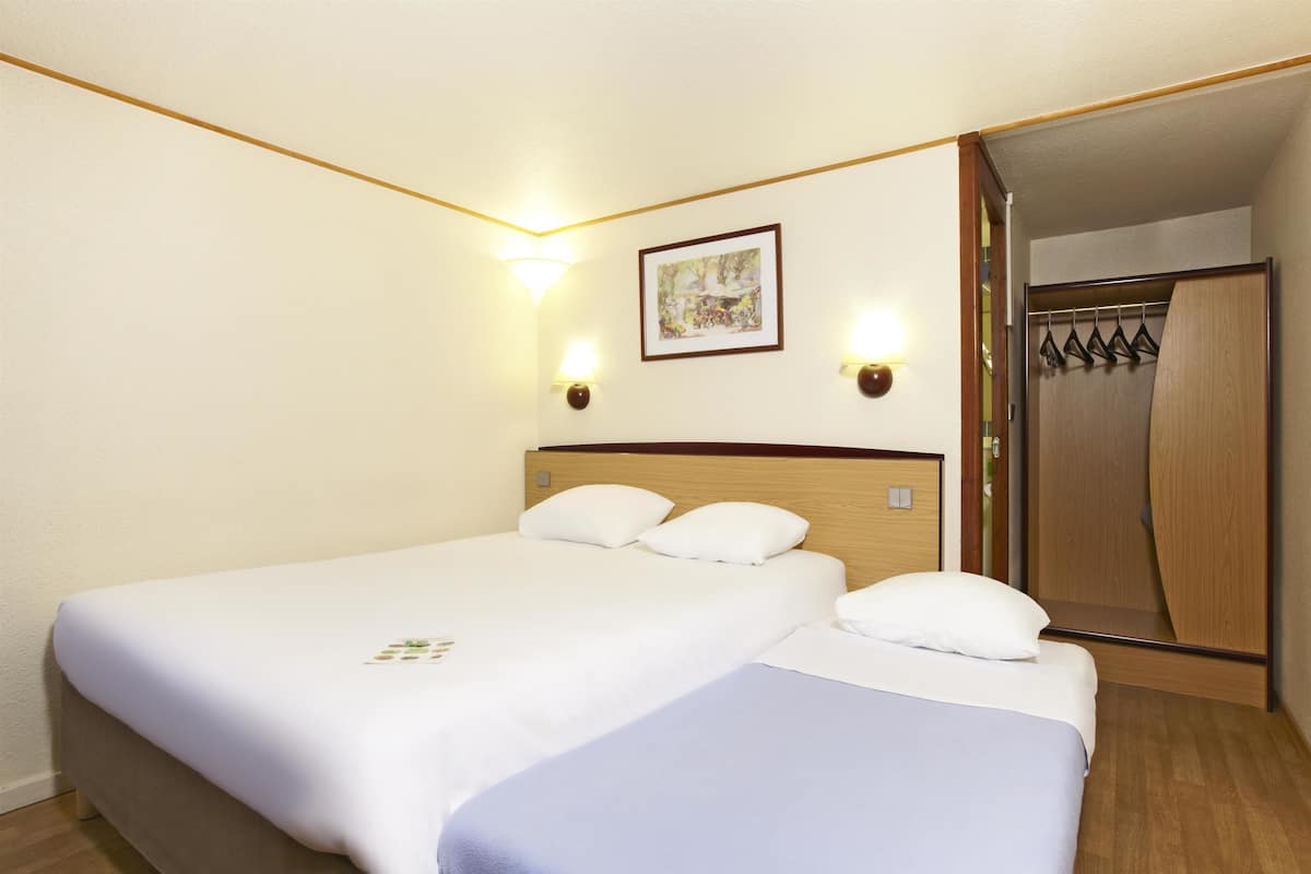 Habitación de hotel con dos camas, cabecero de madera, un cuadro en la pared y un armario con espejo.