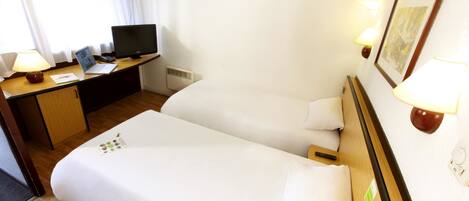 Una habitación de hotel con una cama, un escritorio con una computadora portátil, un televisor y dos lámparas de noche.