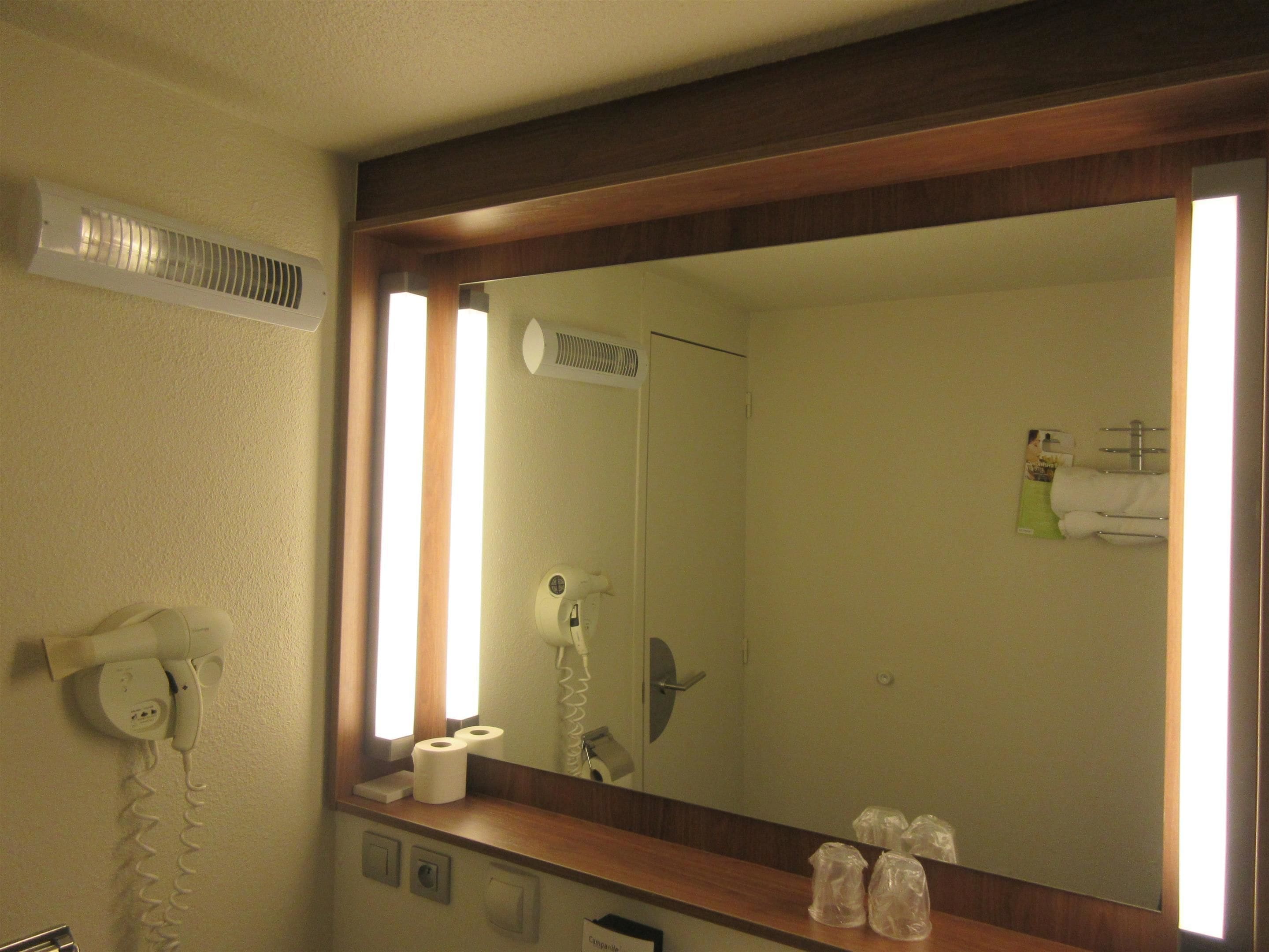 Une salle de bain d’hôtel équipée d’un grand miroir, d’un sèche-cheveux, d’un téléphone et d’un porte-serviettes.