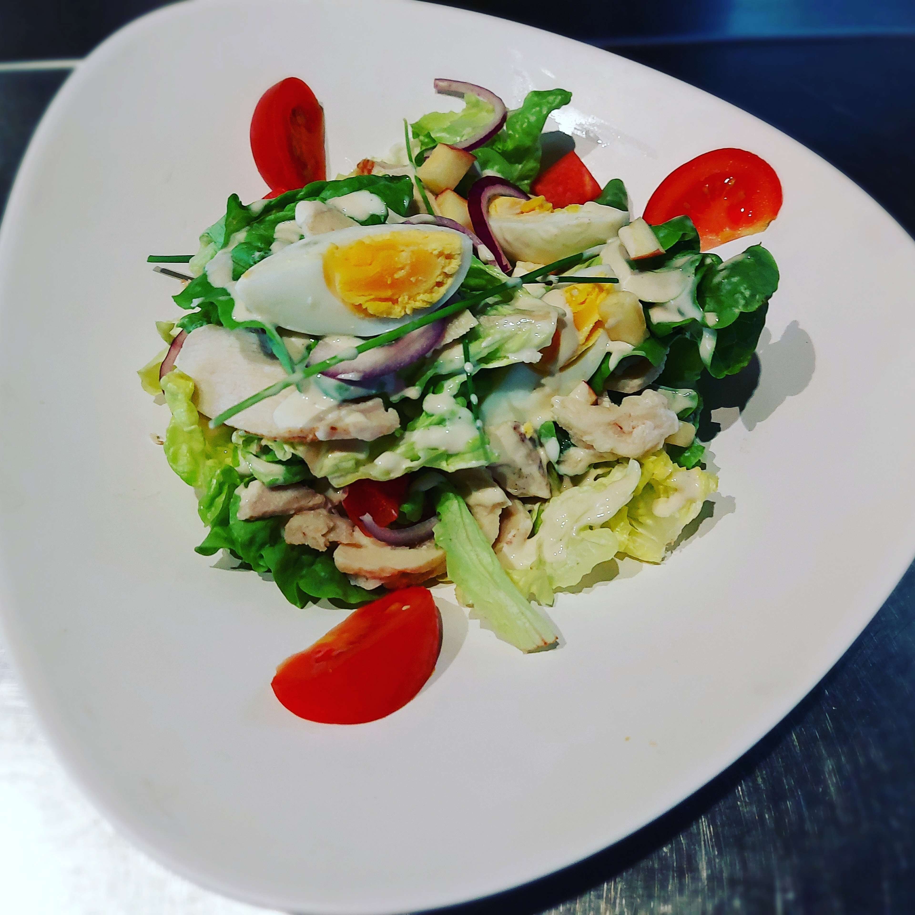 A white plate with a salad containing lettuce, cherry tomatoes, a boiled egg, and slices of meat.