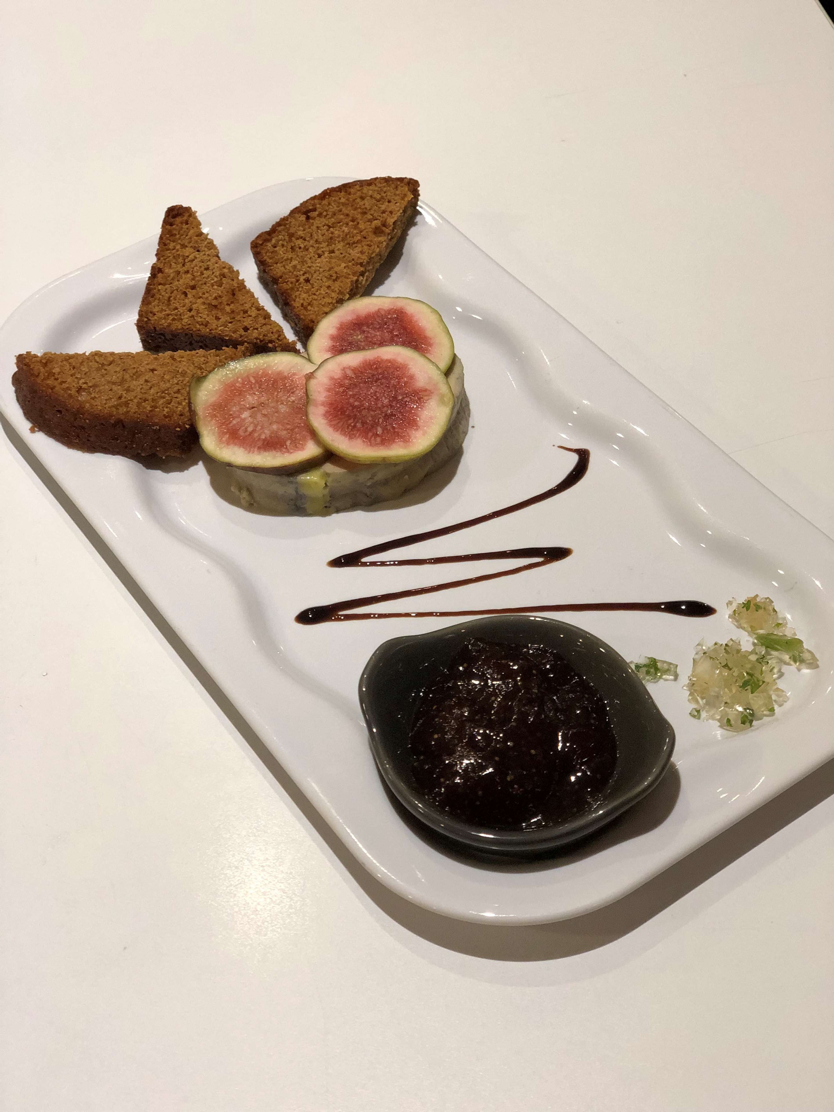 A plate with slices of fig, a small bowl of dark sauce, and some chopped herbs.