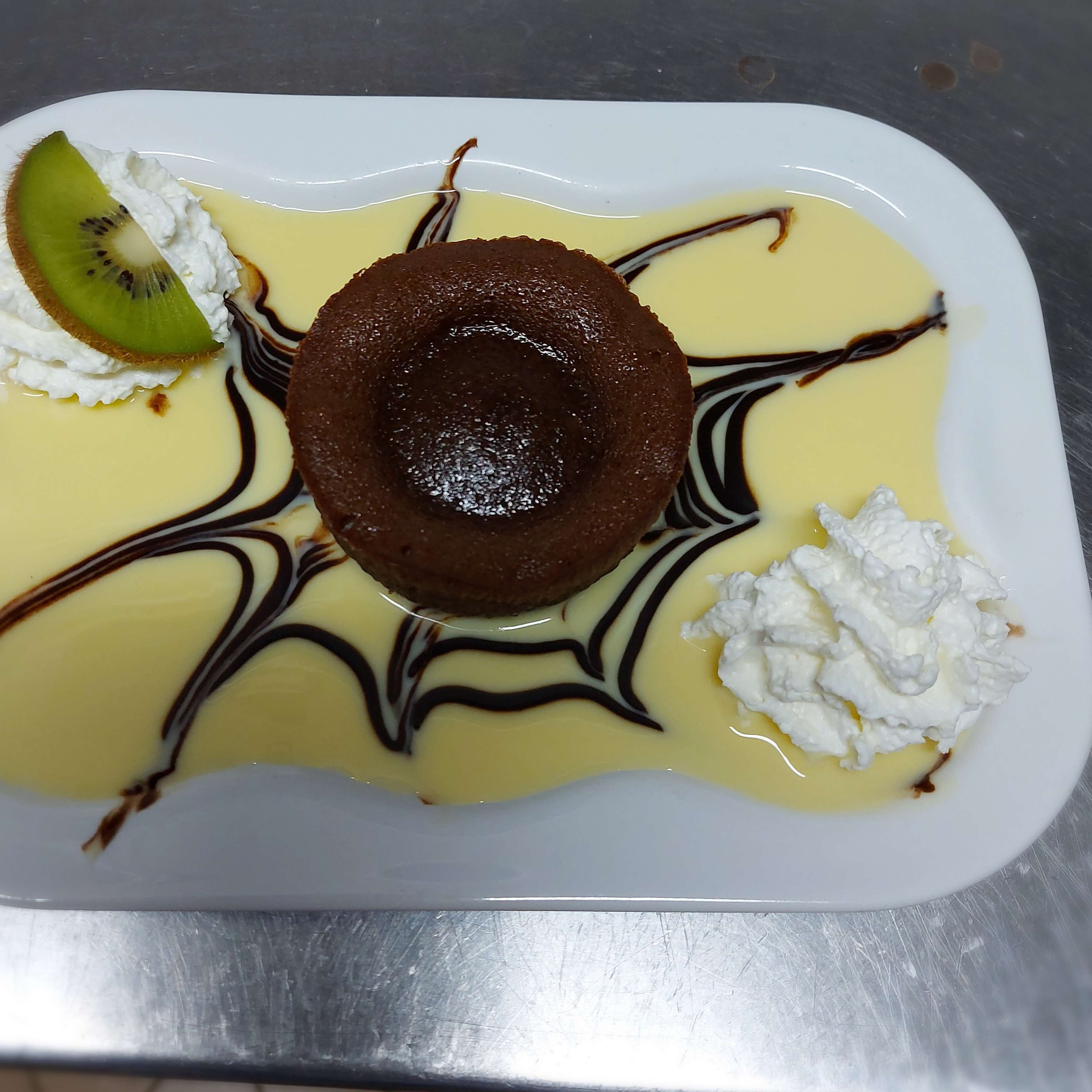 Un plato de postre con un pastel volcán de chocolate, crema batida y una porción de kiwi.