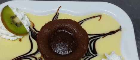 Un plato de postre con un pastel volcán de chocolate, crema batida y una porción de kiwi.