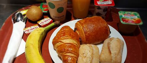 A breakfast tray with croissants, a banana, juice, yogurt, and a coffee cup.