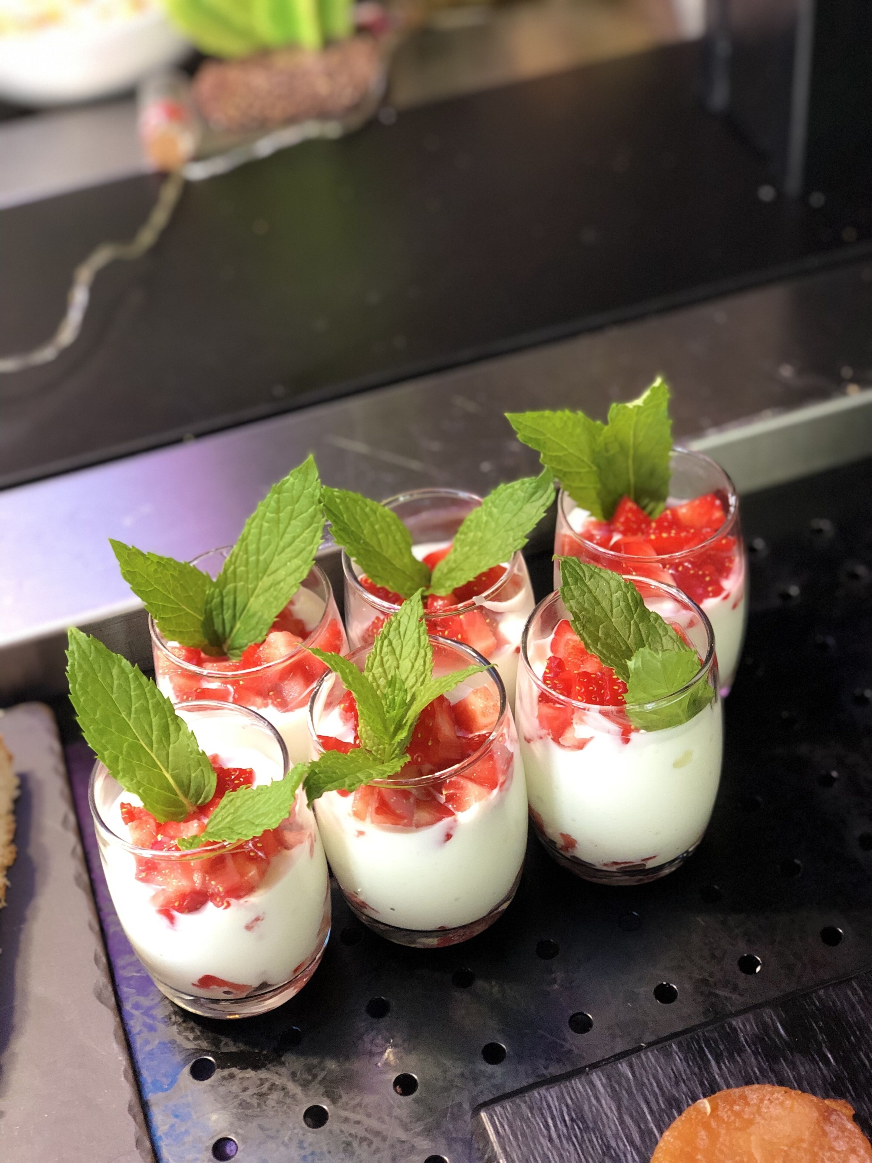 Een schaal met dessertbekers, aardbeien en muntblaadjes.