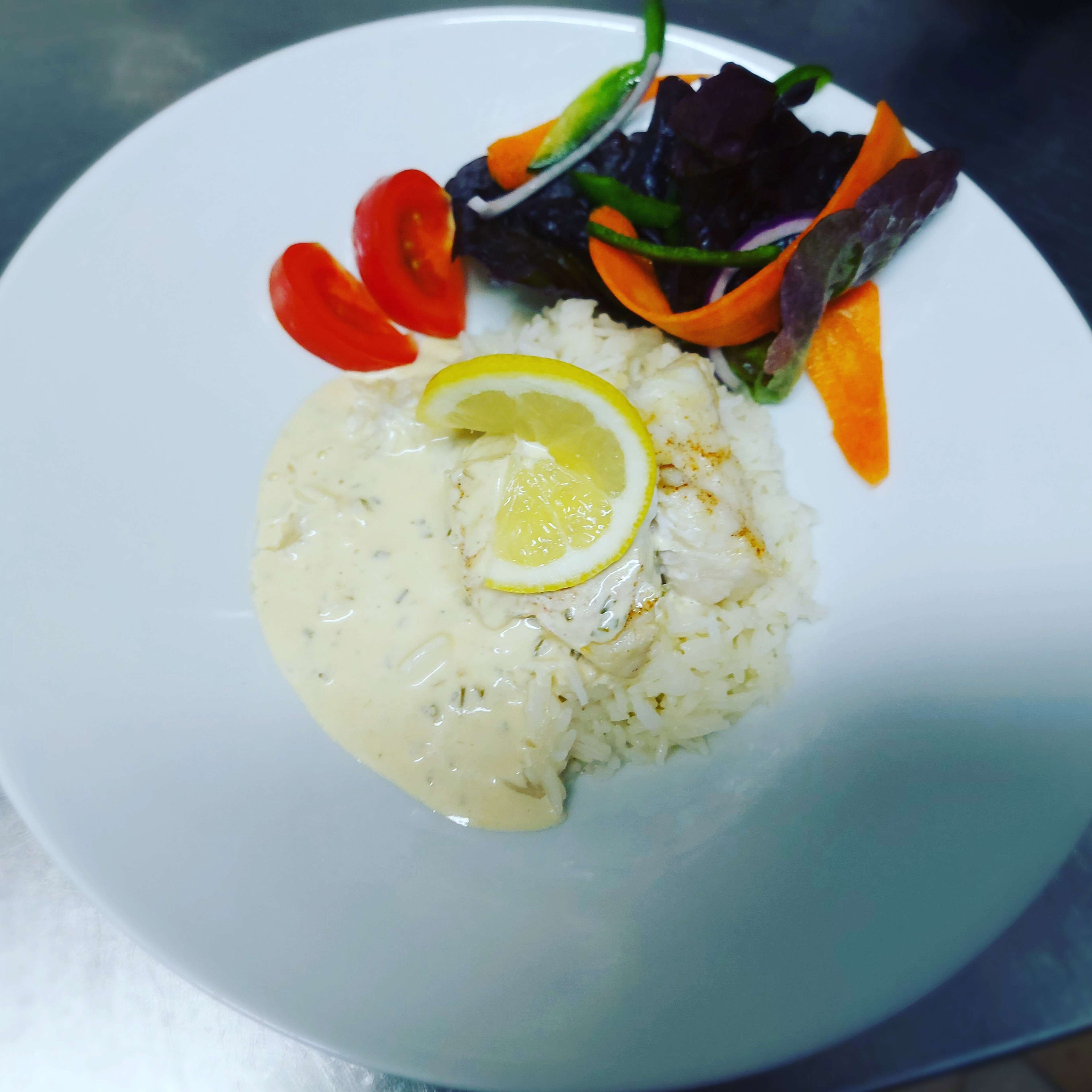 Prato de arroz branco com molho cremoso, decorado com uma fatia de limão, acompanhado por uma salada com folhas verdes e vegetais fatiados.