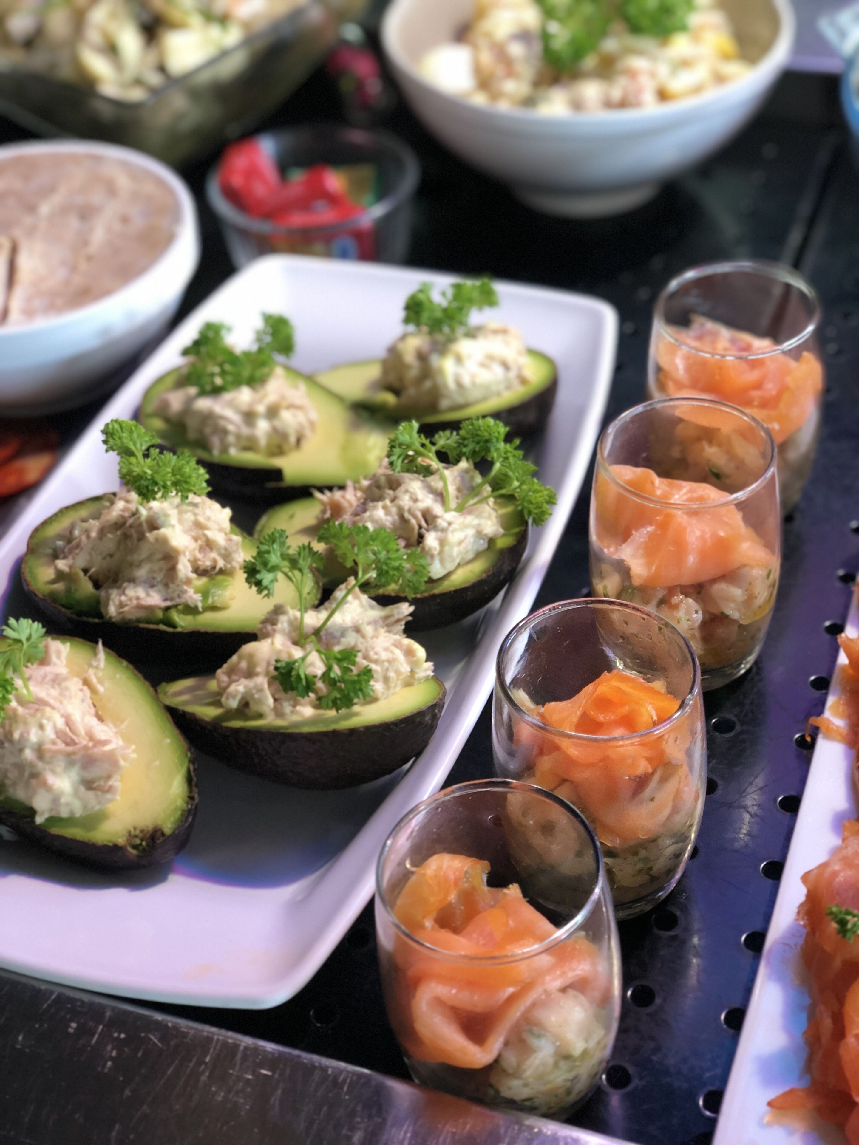 Un vassoio di stuzzichini assortiti con avocado ripieni e bicchieri contenenti salmone.