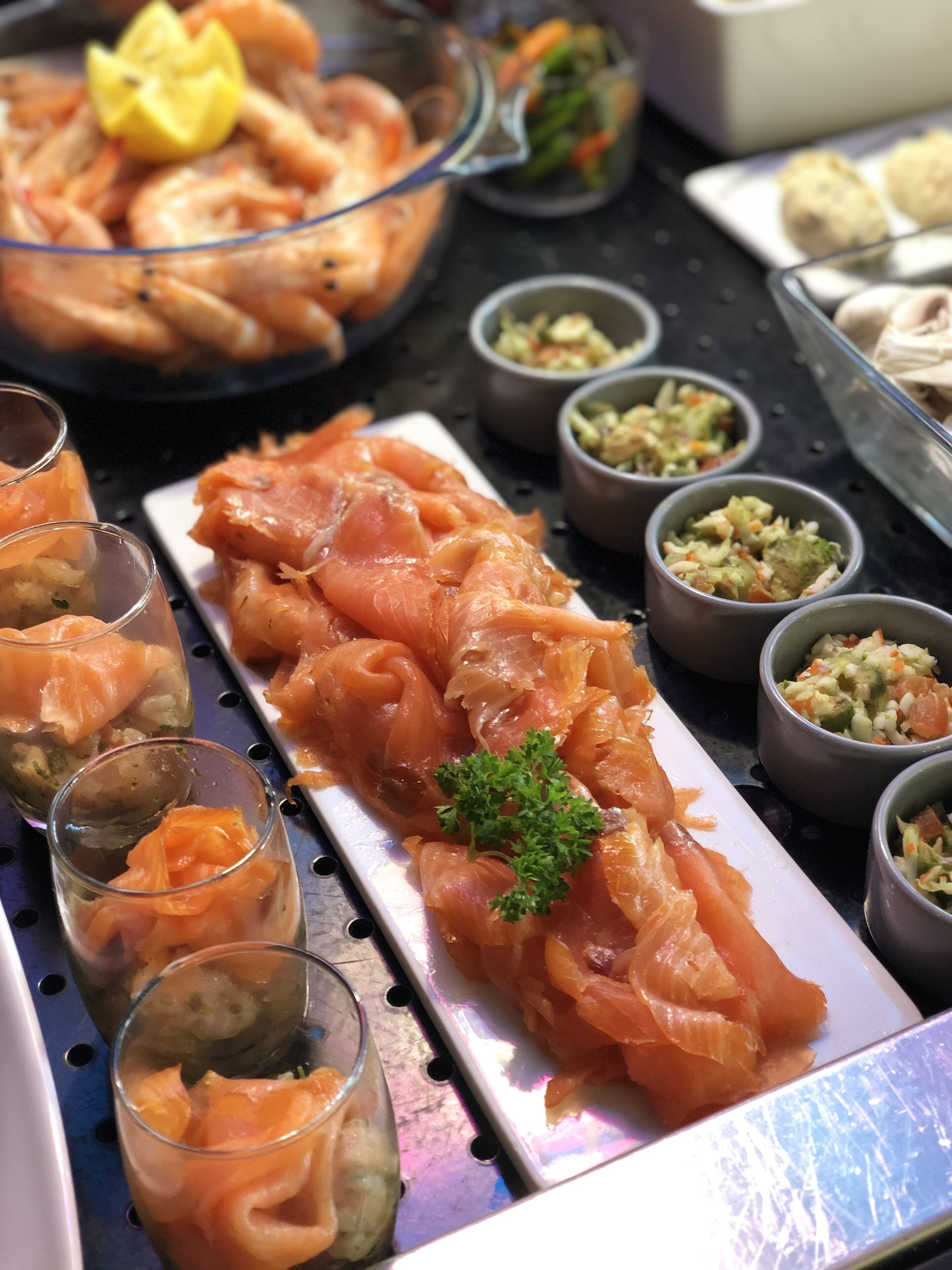 Un buffet proposant une variété de plats, notamment du saumon fumé, des légumes marinés et d’autres petites portions.