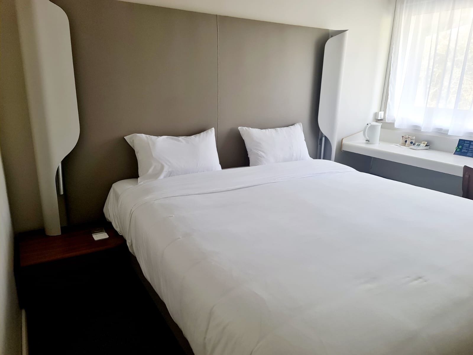 Une chambre d’hôtel avec un grand lit, une table de chevet, une commode et une fenêtre avec des rideaux.