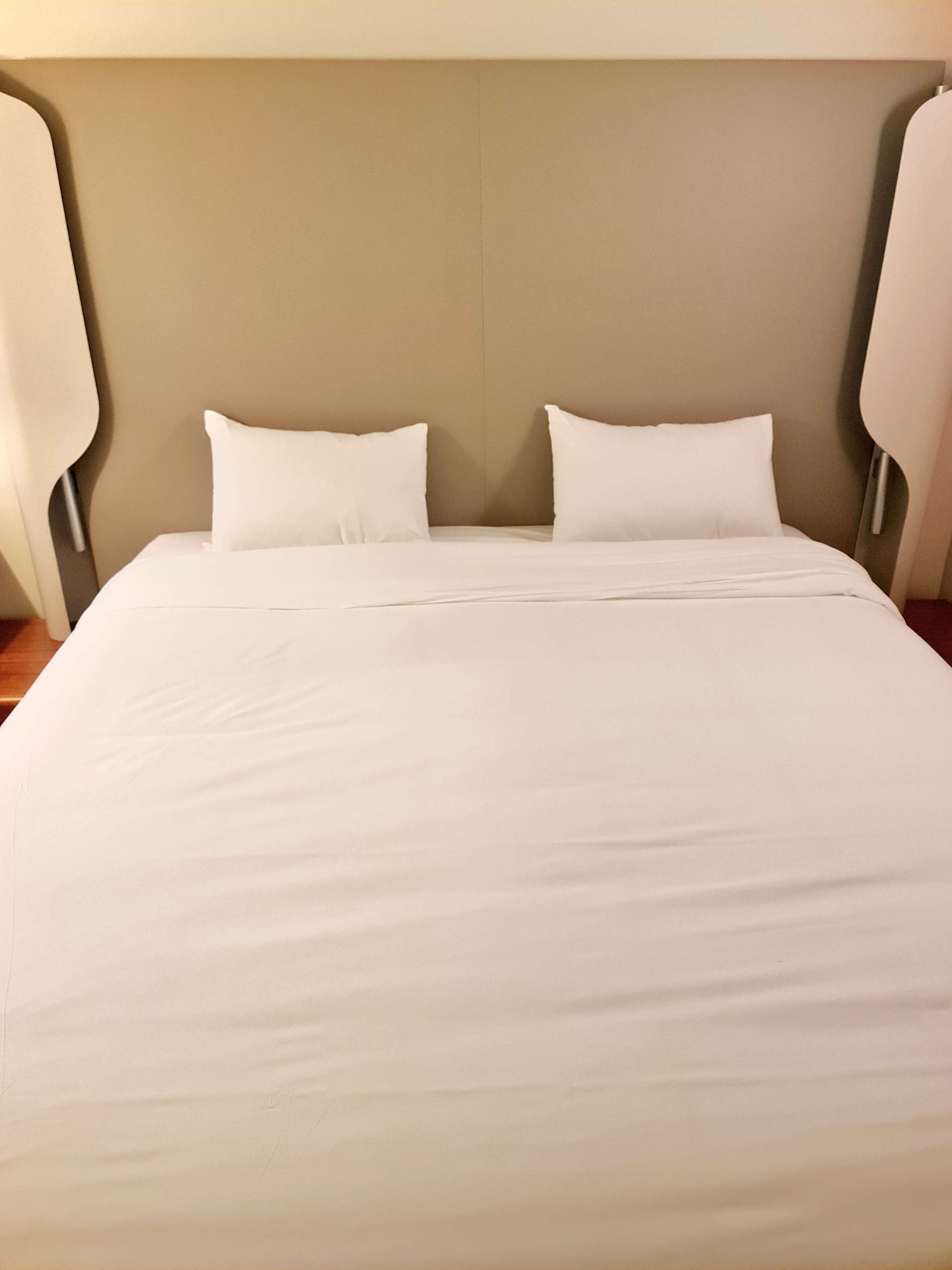 Een net opgemaakt bed met witte lakens en een eenvoudig hoofdbord.