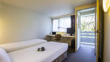 Een hotelkamer met twee eenpersoonsbedden, een bureau met een computer, een stoel en uitzicht op de omgeving via een deur.