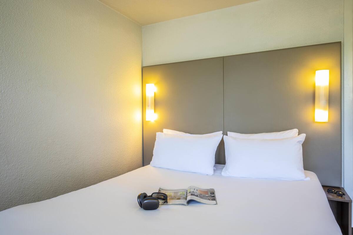 Un lit bien fait, avec des draps blancs, deux oreillers, une paire d’écouteurs et un magazine posés sur le lit.