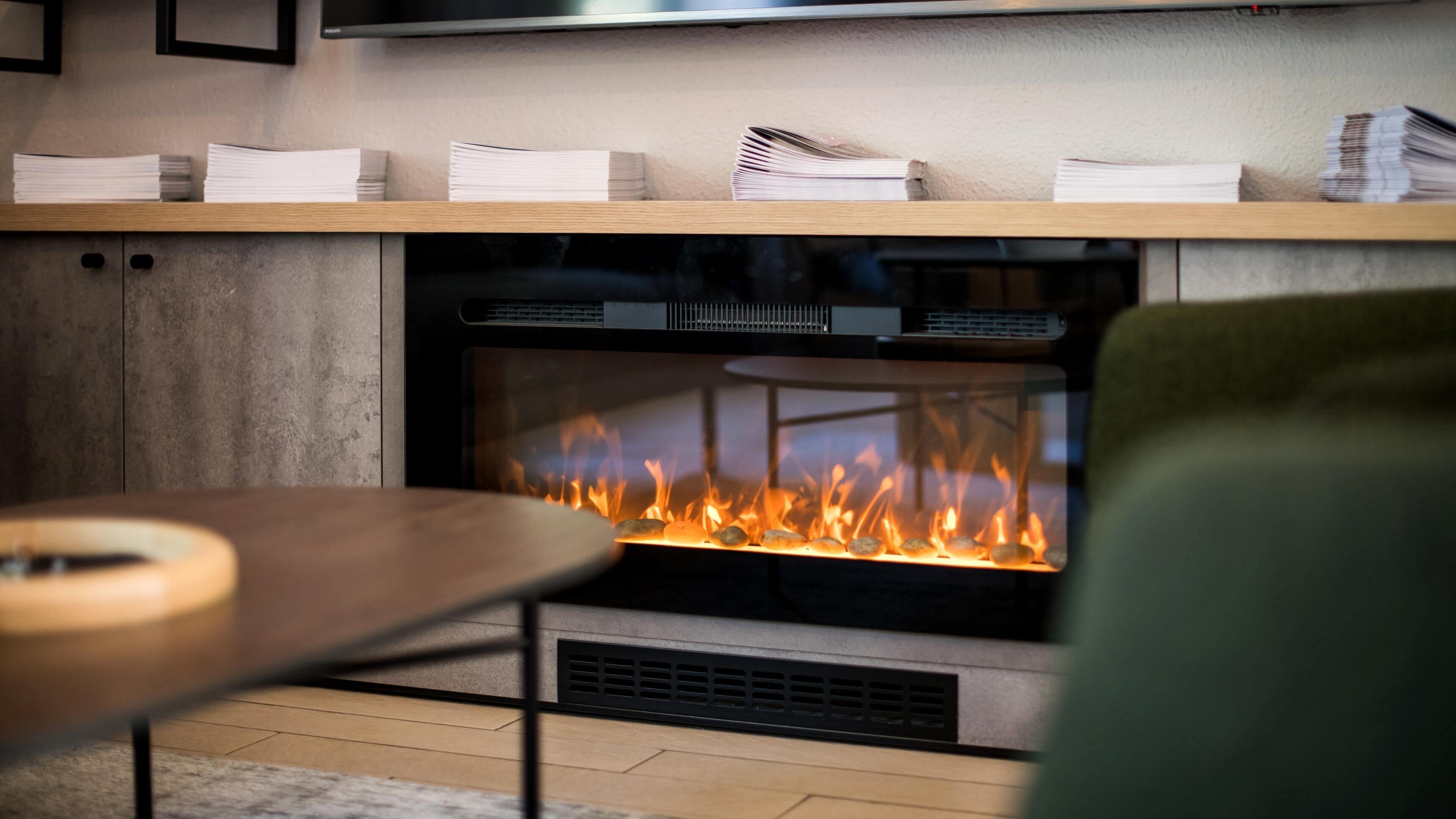 Una chimenea moderna con fuego a la vista, un estante de madera encima y una mesa en primer plano.