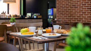 A breakfast setting with a table set for two, including plates with food, a glass of orange juice, a cup of coffee, and a pastry.