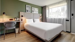 Une chambre d’hôtel avec un lit, un bureau, une chaise, une poubelle et deux tableaux encadrés au mur.