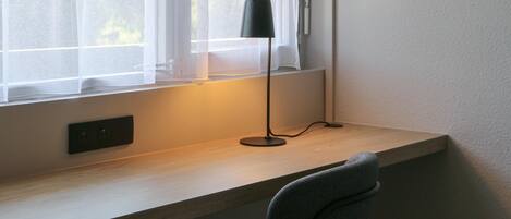 A desk with a lamp, a chair, and a window with sheer curtains.