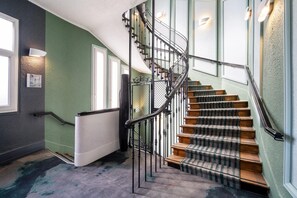 A spiral staircase with a metal railing, carpeted stairs, and a radiator on the wall. - Best Western Dijon Centre Gare (Dijon)