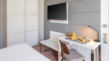 A modern hotel room with a bed, a desk with breakfast, a TV, and a power outlet.