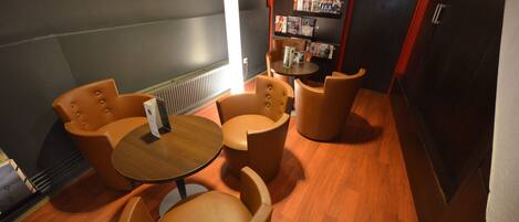 A cozy lounge area with leather armchairs and a small round table, a magazine rack, and a door with a sign.