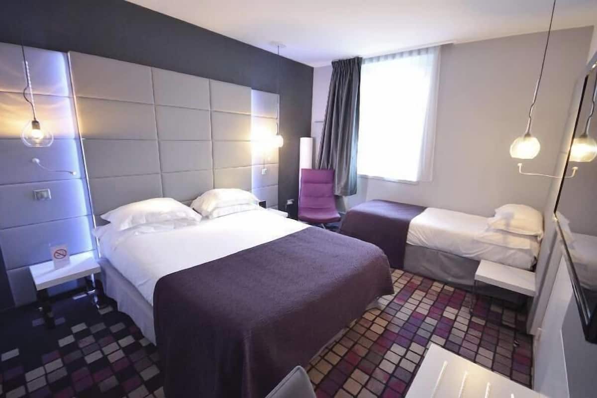 Quarto de hotel com uma cama grande, uma cama menor, uma escrivaninha e uma cadeira.