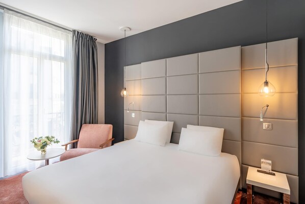 A hotel room with a large bed, a chair, a small table with a vase, and a nightstand with a remote control. - Best Western Dijon Centre Gare (Dijon)