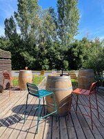 Una terraza de madera con sillas de metal y un barril de vino.